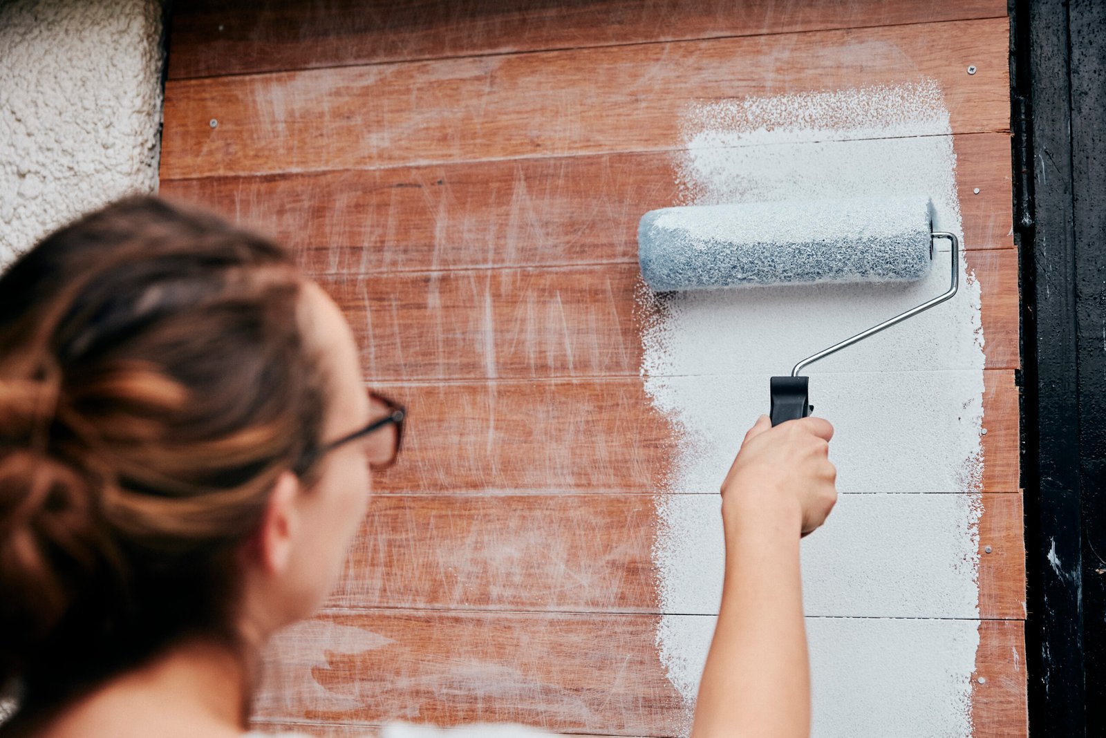 A craftsman meticulously applies paint to the exterior of a charming house with fresh landscaping, highlighting the transformative power of professional painting.